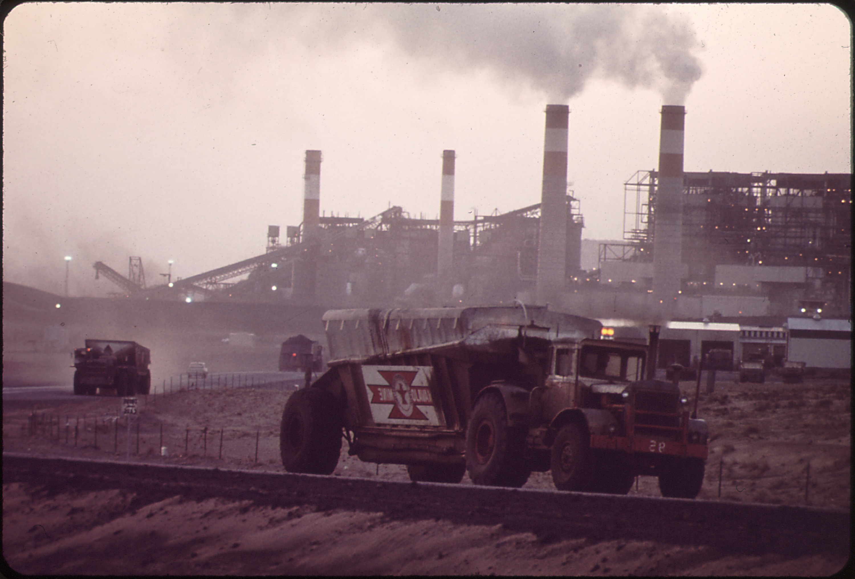 Historical photograph H3. Trucks hauling coal from Navajo Mine to Four Corners Generating Plant, May 1972. Trucks, transport route, and generating plant reveal the physical connection behind a continuing supply relationship. Lyntha Scott Eiler, EPA/DOCUMERICA; NARA 544169.