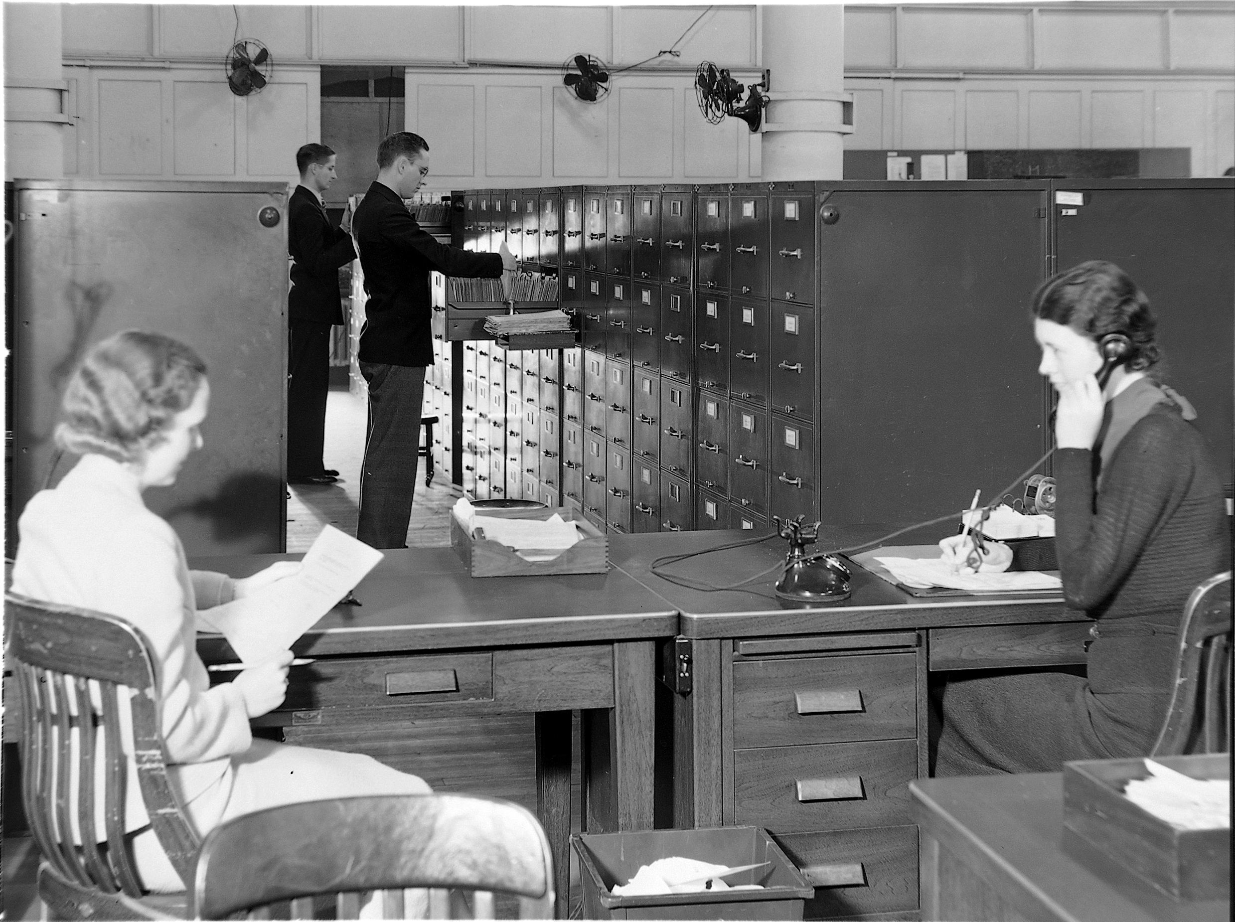 Historical photograph H5. TVA central files, titled 1936 in the archive: staff retrieve folders, handle documents, and use a telephone among indexed cabinets. TVA Web Team, K-0897.